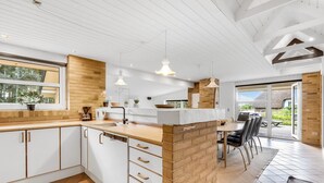 A modern kitchen with white cabinets, a brick accent wall, and a dining area with a table and chairs. - "Ewy" - 300m from the sea by Interhome (Ringkøbing)