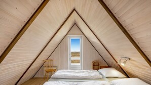 Une petite chambre mansardée de forme triangulaire, avec deux lits, une chaise en bois et une porte donnant sur un paysage pittoresque.