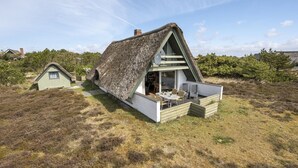 Une maison à toit de chaume, dotée d’un toit en pente, d’un espace repas avec des sièges en plein air et d’un bâtiment plus petit attenant.