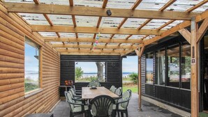 A covered patio with a wooden table and chairs, a view of the outdoors, and a building with large windows. - Vacation home "Graa" by Interhome (Skanderborg)