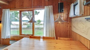 A wooden interior with a large dining table, two pendant lights, and a view of the outdoors. - Vacation home "Graa" by Interhome (Skanderborg)