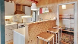 A compact kitchen with wooden walls, a central island, bar stools, and a bunk bed in the adjacent room. - Vacation home "Graa" by Interhome (Skanderborg)