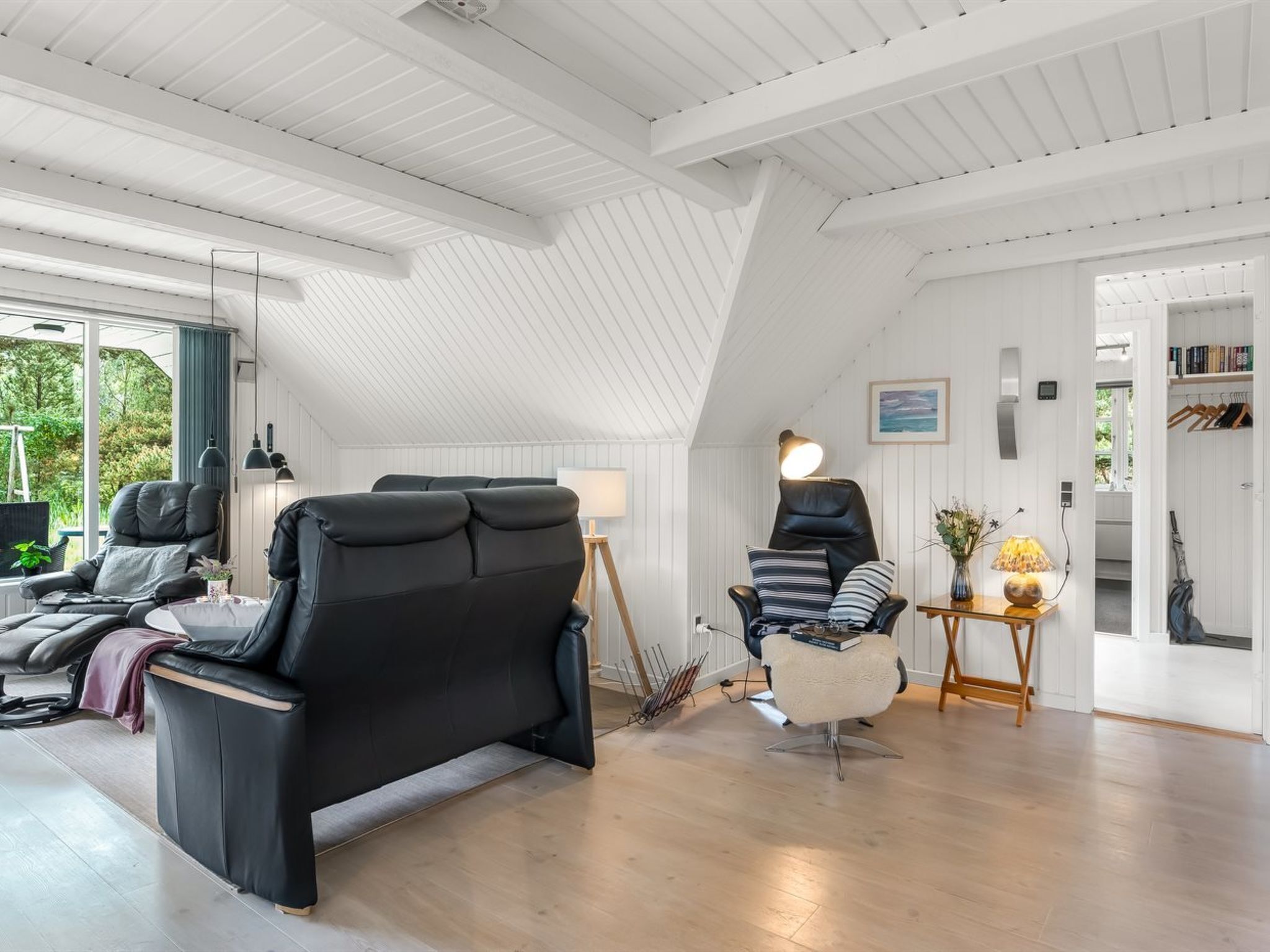 Un intérieur moderne avec un plafond en pente, un canapé en cuir noir, une chaise blanche et une petite table avec une lampe.