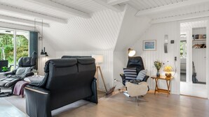 A modern interior with a sloped ceiling, a black leather sofa, a white chair, and a small table with a lamp.