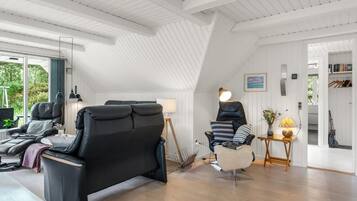 Un intérieur moderne avec un plafond en pente, un canapé en cuir noir, une chaise blanche et une petite table avec une lampe.