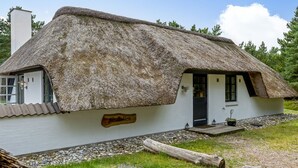 A traditional thatched-roof house with a white exterior, a wooden sign, and a gravel path leading to the entrance.