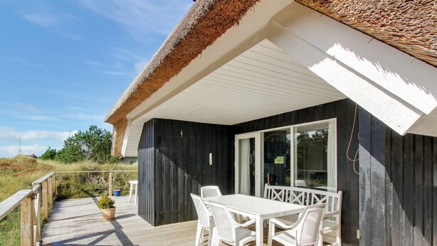 A covered outdoor area with a wooden deck, white plastic chairs, and a table.
