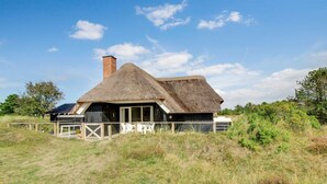 A thatched-roof house with a wooden deck and a fenced outdoor area.