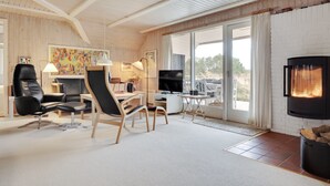 A modern living room with a fireplace, wooden ceiling beams, and large windows.