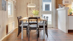 A dining area with a wooden table and chairs, a hanging light fixture, and a view of the outdoors through a door.
