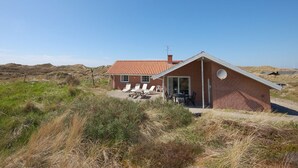 A two-story brick house with a red-tiled roof, a covered patio with lounge chairs, and a sandy landscape. - "Riborg" -  from the sea by Interhome (Ringkøbing)