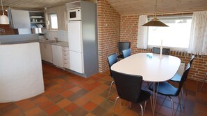 A compact kitchen with a refrigerator, microwave, and sink. There is a dining area with a table and chairs. - "Riborg" -  from the sea by Interhome (Ringkøbing)