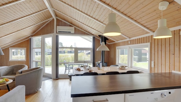 Una cucina moderna con una grande isola, soffitto in legno e ampie finestre che offrono vista sull'esterno.