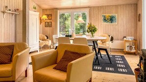 Una habitación acogedora con paredes de madera, una zona de comedor con una mesa y sillas, un sofá con cojines y una chimenea.