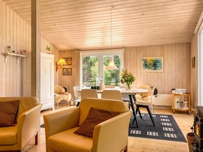 A cozy room with wooden walls, a dining area with a table and chairs, a sofa with cushions, and a fireplace.