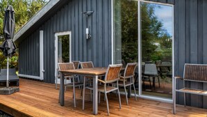 Una terraza moderna al aire libre con una mesa y sillas de madera, un portón corredero de vidrio y una barandilla de metal.