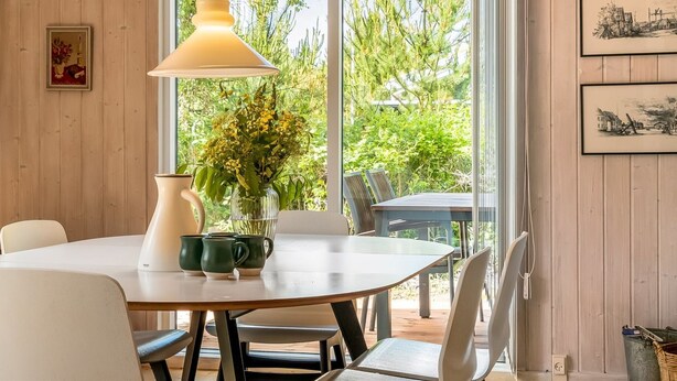 Un comedor con una mesa redonda, sillas, un florero con flores, una lámpara y cuadros en la pared.
