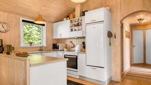 Una cocina con armarios blancos, estufa, refrigerador y ventana con vista a zonas verdes.
