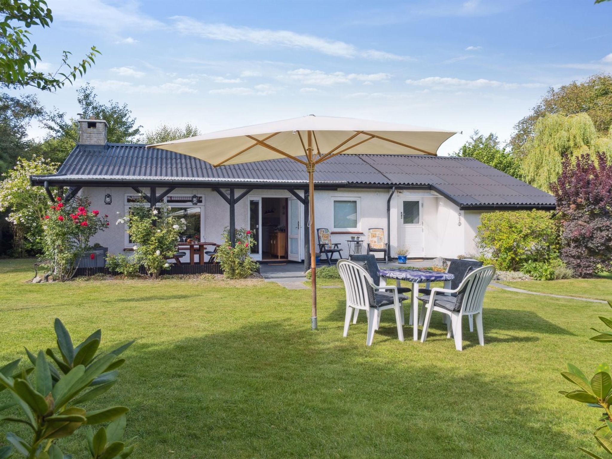 Een huis met een overdekt terras, een gazon en een tuin.