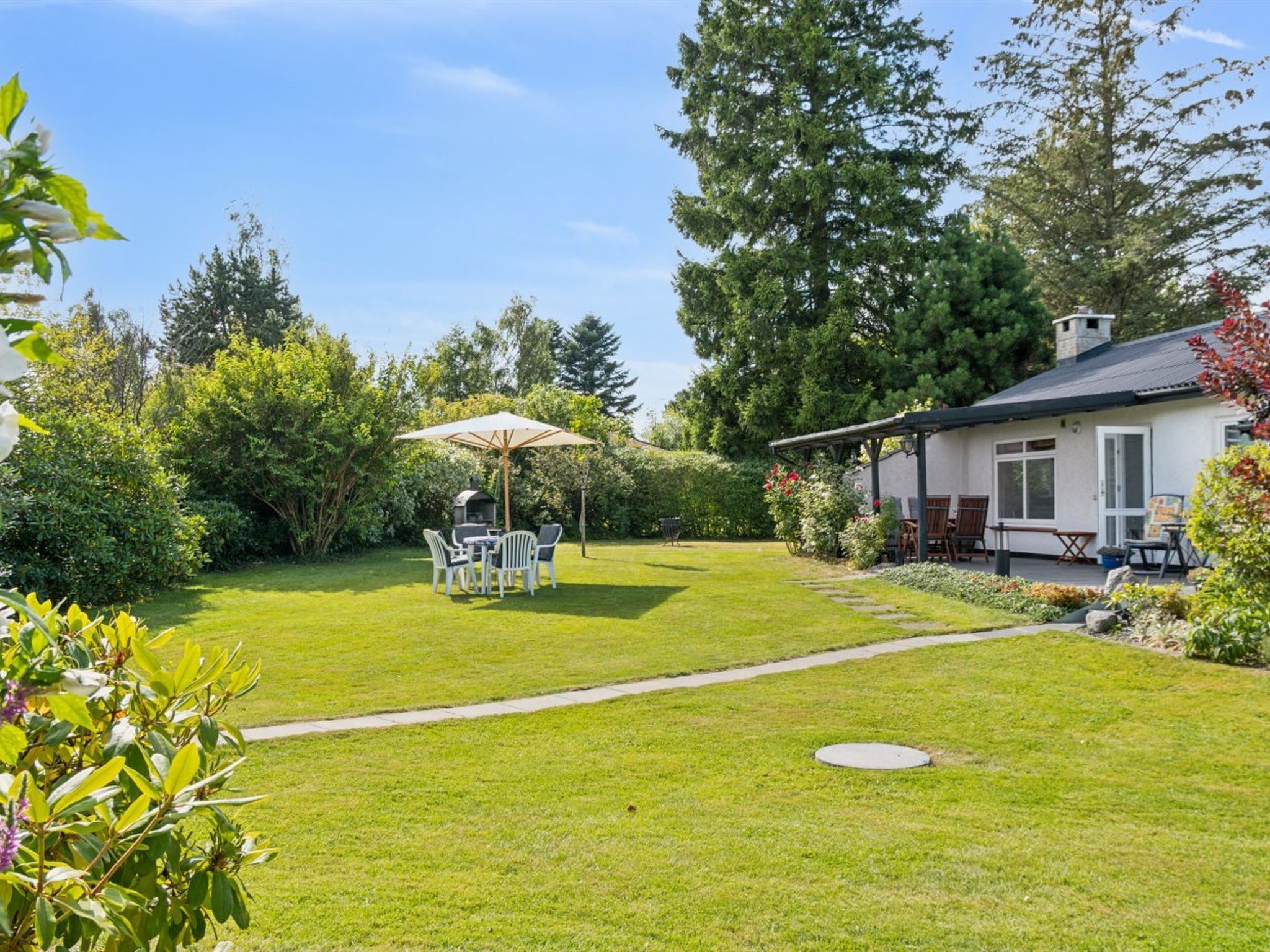Un jardin bien entretenu avec une terrasse, un espace salon extérieur et un coin barbecue.