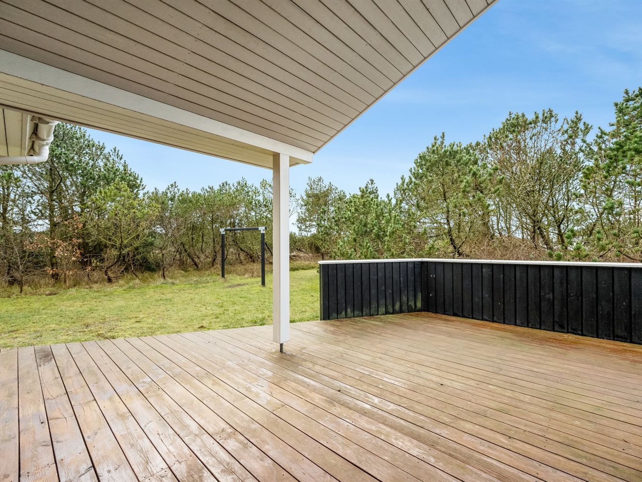 Eine Holzterrasse mit überdachtem Bereich, umgeben von Bäumen und einer grünen Wiese.