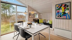 Een moderne eetruimte met een witte tafel, zwarte stoelen en hanglampen. Een groot raam biedt uitzicht op de omgeving.