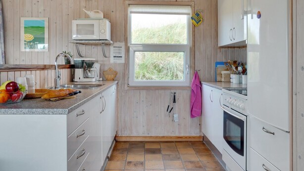 Eine kleine Küche mit Holzwänden, einem Fenster, einer Mikrowelle, einer Kaffeemaschine und einem Herd.