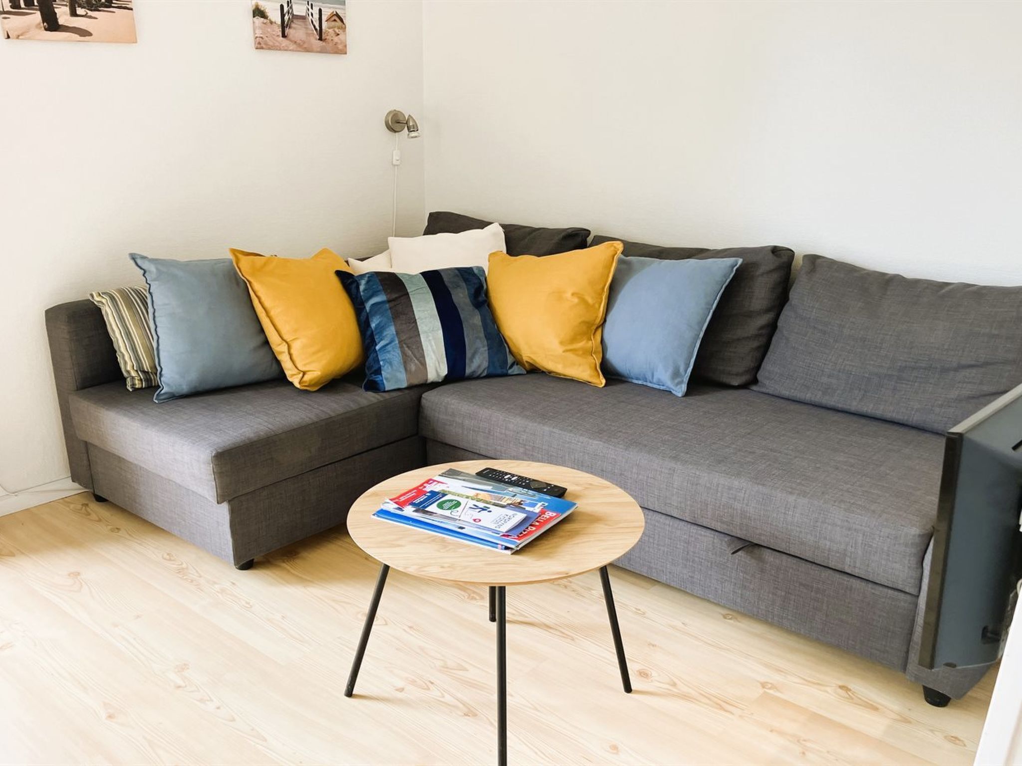 Un salon moderne avec un canapé d’angle gris, une petite table basse ronde en bois et un luminaire fixé au mur.