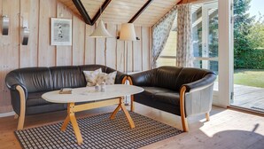 Ett mysigt rum med ett träpanelat tak, en svart lädersoffa, ett litet runt bord och utsikt över omgivningen genom en glasdörr.
