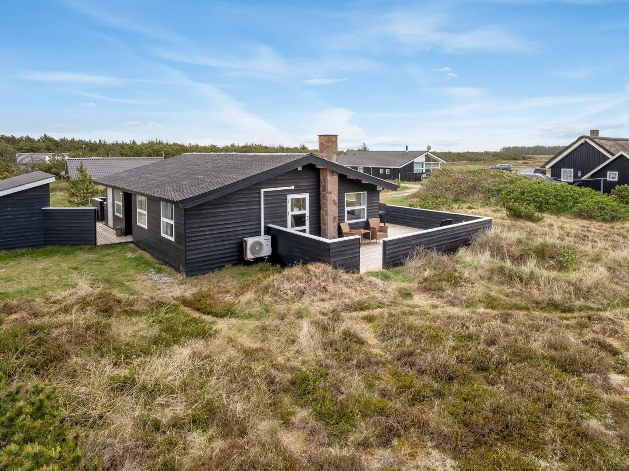 A modern house with a large deck, surrounded by natural landscape.