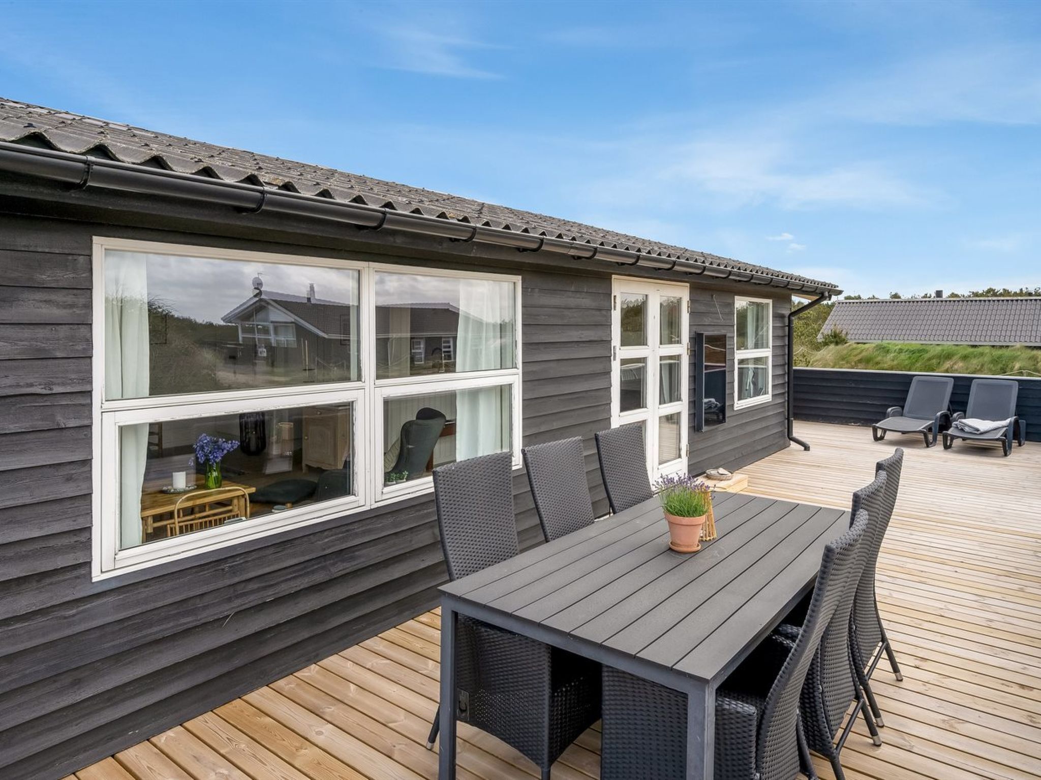 A wooden deck with a table and chairs, large windows, and a view of the landscape.