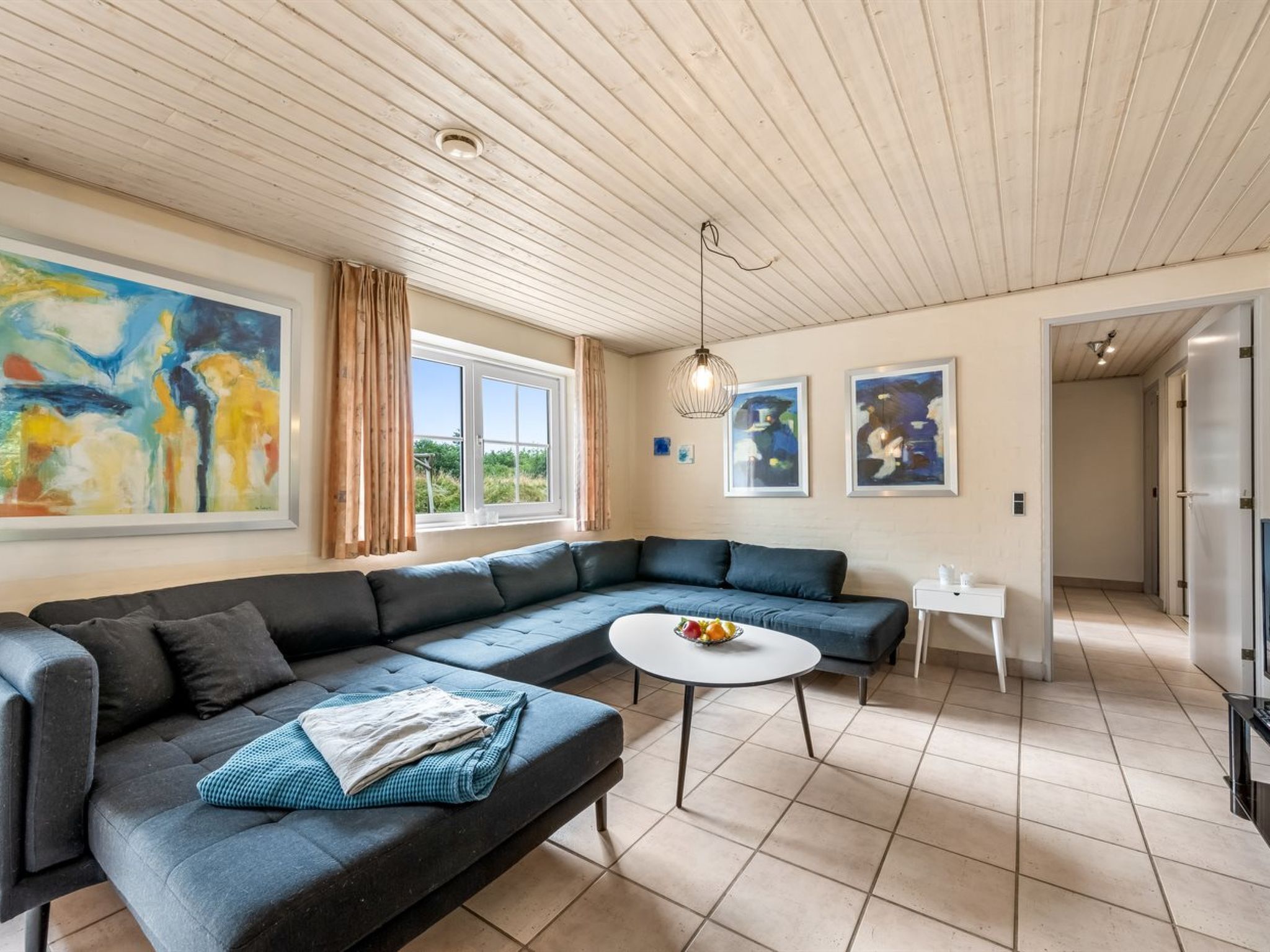 Ein modernes Wohnzimmer mit einem Ecksofa, einem runden Couchtisch und Blick ins Freie durch ein Fenster.