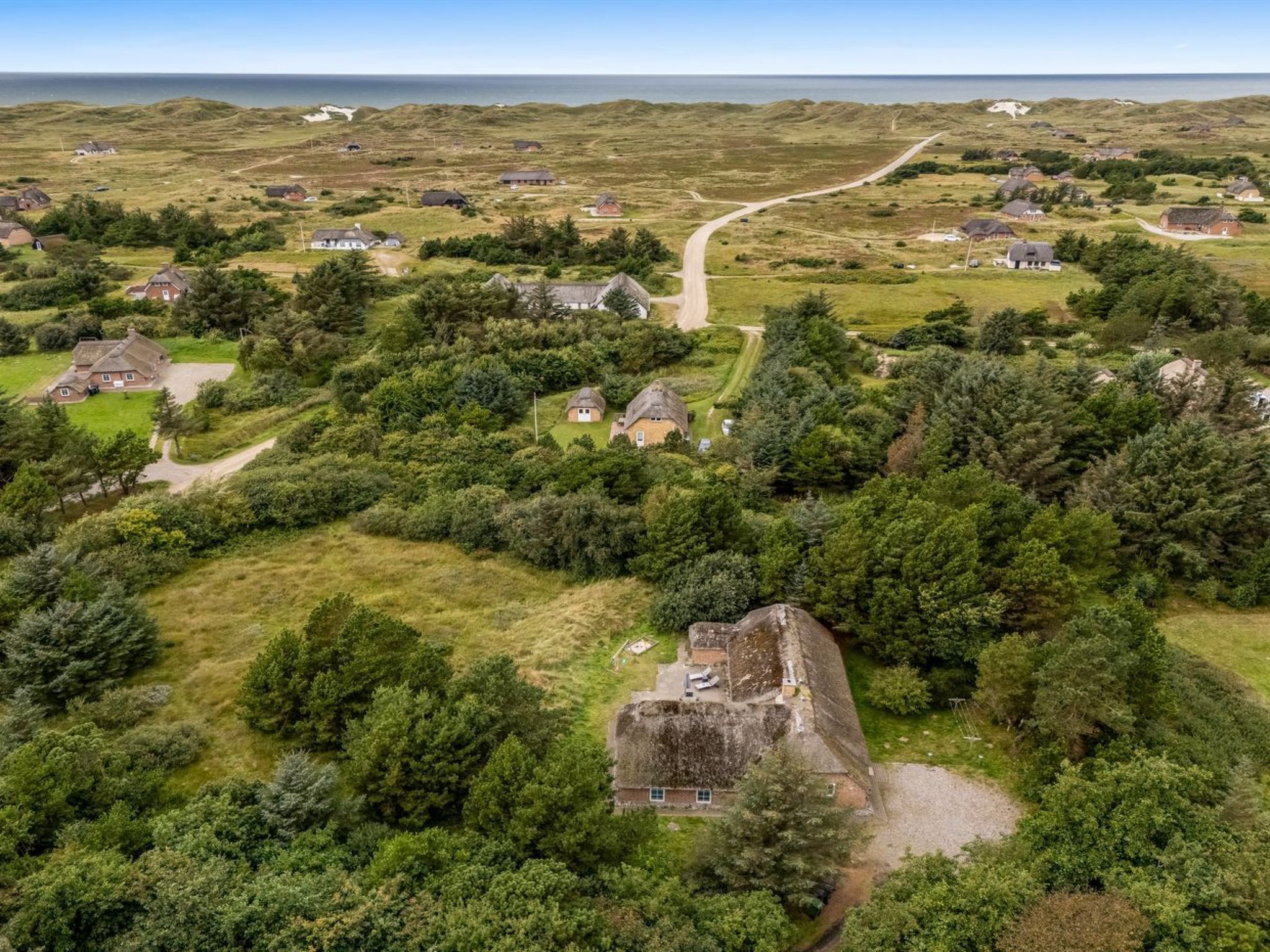 Eine Vogelperspektive auf eine ländliche Gegend mit Häusern, einer markanten Steinarchitektur und einer Straße, die zum Meer führt.