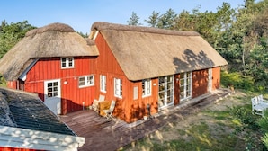 Et rødt træhus med stråtækt tag, en træterrasse og et lille haveområde.