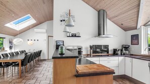 Une cuisine moderne avec un plafond en bois, une lucarne, un îlot central et un coin repas avec des chaises.