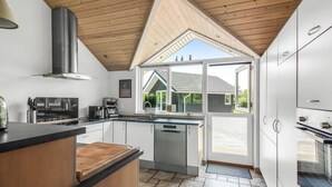 Une cuisine moderne avec un plafond en bois, une grande fenêtre et une vue sur une maison.