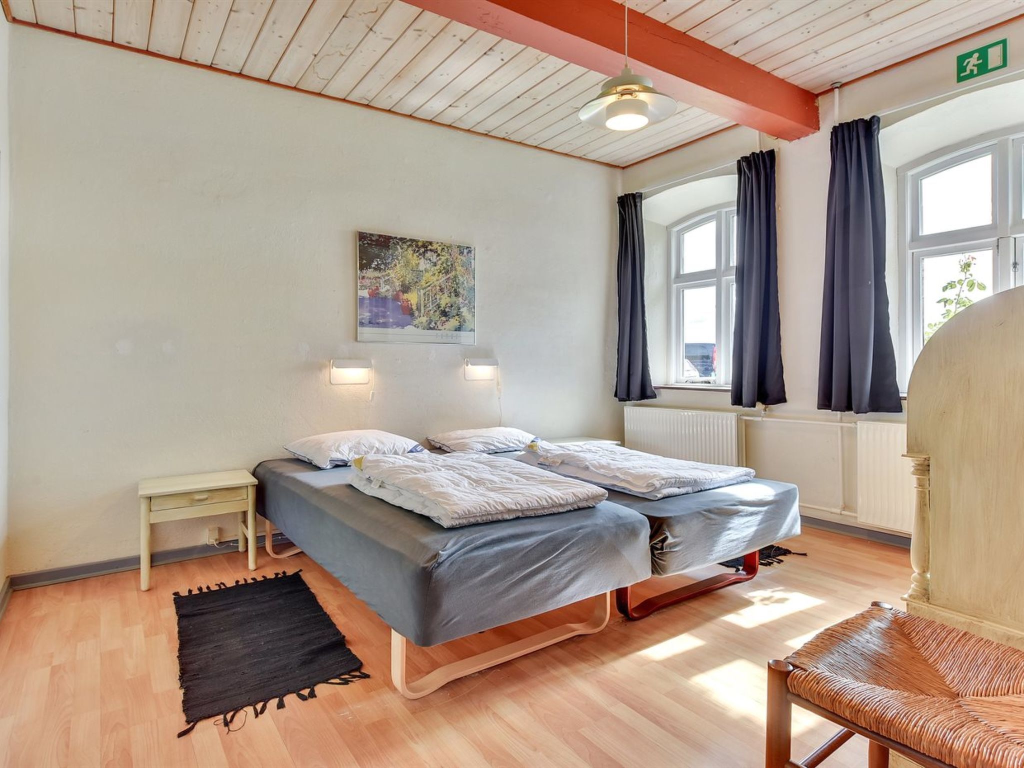 Une pièce comprenant un lit, une chaise, une petite table, un tableau et une fenêtre avec des rideaux.