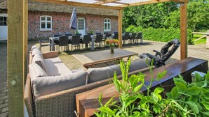 A covered outdoor seating area with tables and chairs, a wicker sofa, and a grill. - "Tilla" - 600m from the sea by Interhome (Bredebro)