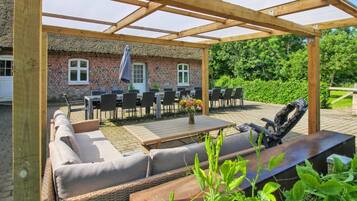 Un espace extérieur aménagé, abrité et doté de tables et de chaises, d’un canapé en osier et d’un barbecue.