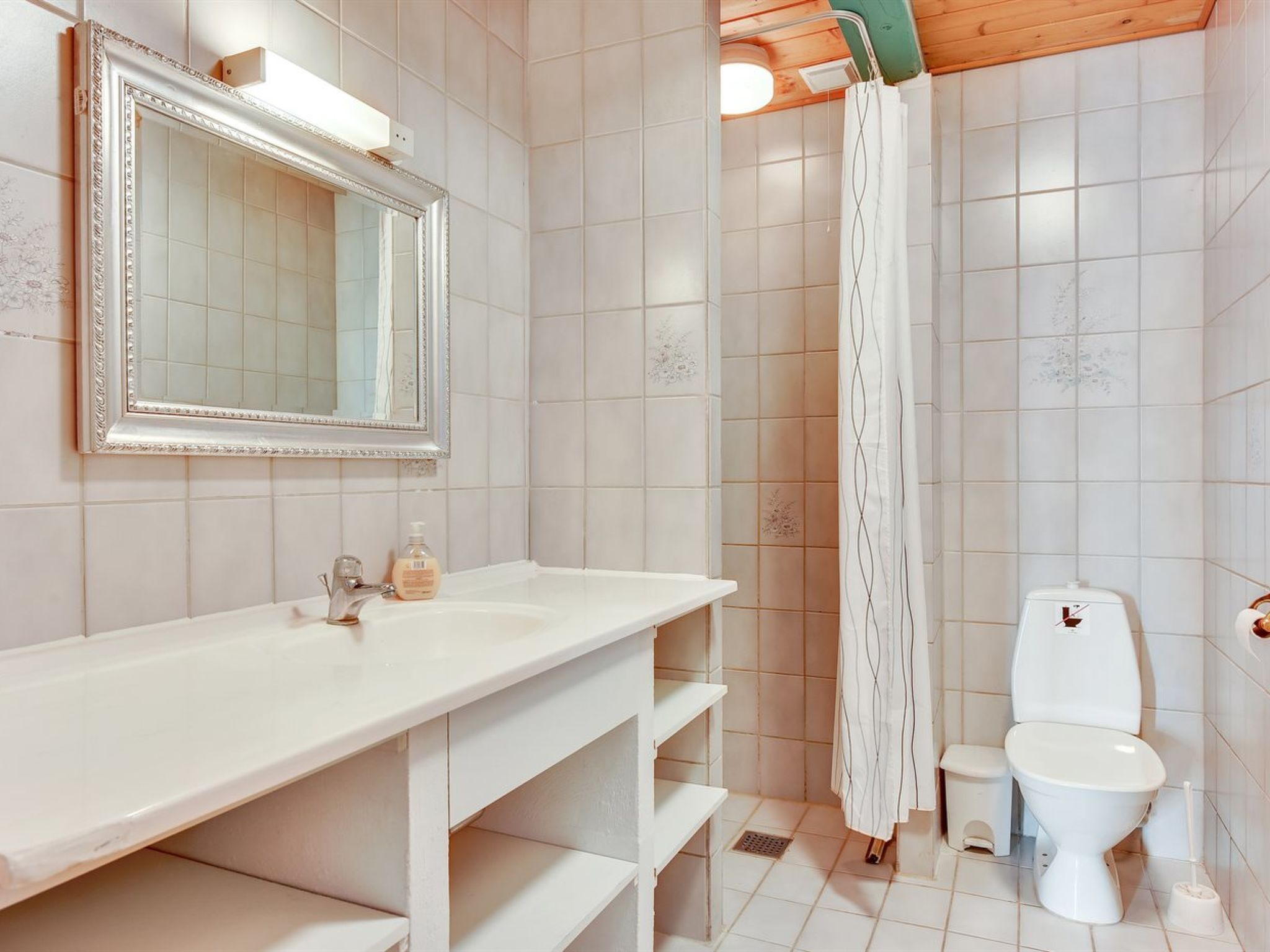 Un baño con lavamanos blanco, espejo, inodoro y cortina de ducha.