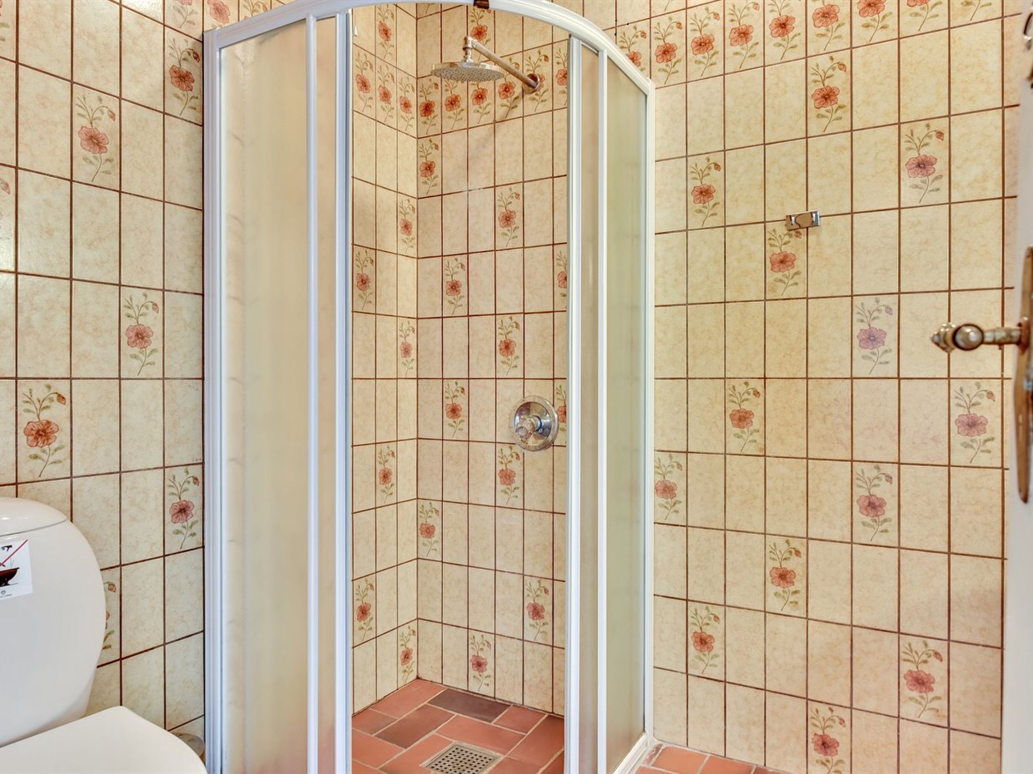 A shower with a glass door, tiled walls with floral patterns, and a visible showerhead.
