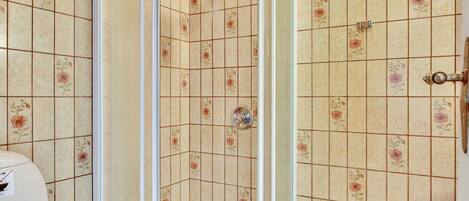 A shower with a glass door, tiled walls with floral patterns, and a visible showerhead.