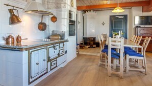 A kitchen with white cabinetry, copper pots, a central island, and a dining area with wooden chairs and a blue tablecloth. - "Tilla" - 600m from the sea by Interhome (Bredebro)