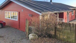 Een rood houten huis met een metalen dak, schoorsteen en een klein terras.