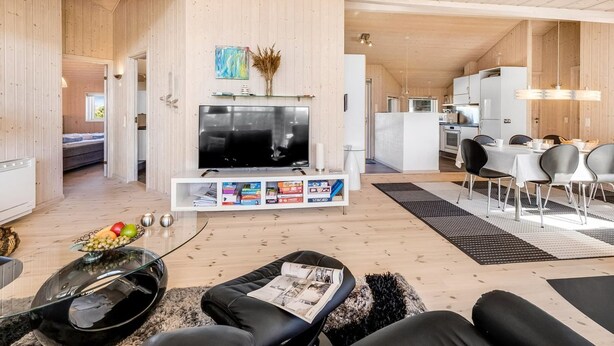 Uma sala de estar moderna com televisão de tela plana, estante de livros e área de jantar com mesa e cadeiras.