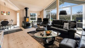 Uma sala de estar moderna com lareira a lenha, mobiliário de couro e grandes janelas com vista para o exterior.