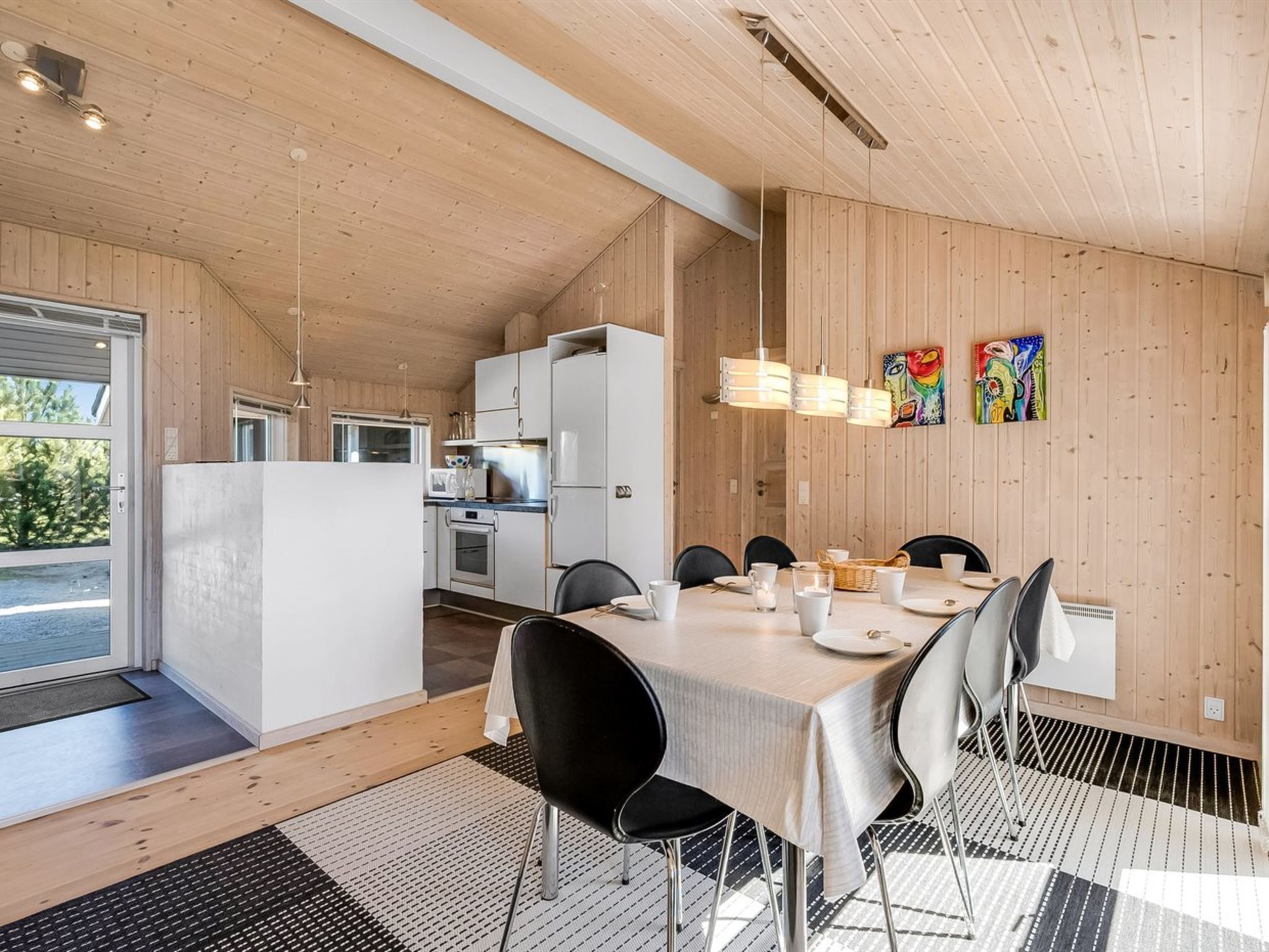 Una cocina moderna con armarios blancos, un comedor con una mesa dispuesta para cuatro personas y vistas al exterior.