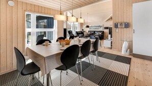Uma sala de jantar moderna com mesa de madeira, cadeiras pretas e luminárias pendentes.