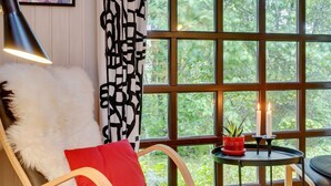 Un coin salon confortable avec un fauteuil, un coussin moelleux et un coussin rouge. Une lampe noire est posée sur une table à côté du fauteuil.