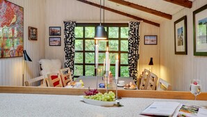 Un coin repas avec une table en bois, des chaises, un saladier de fruits et un verre à vin.